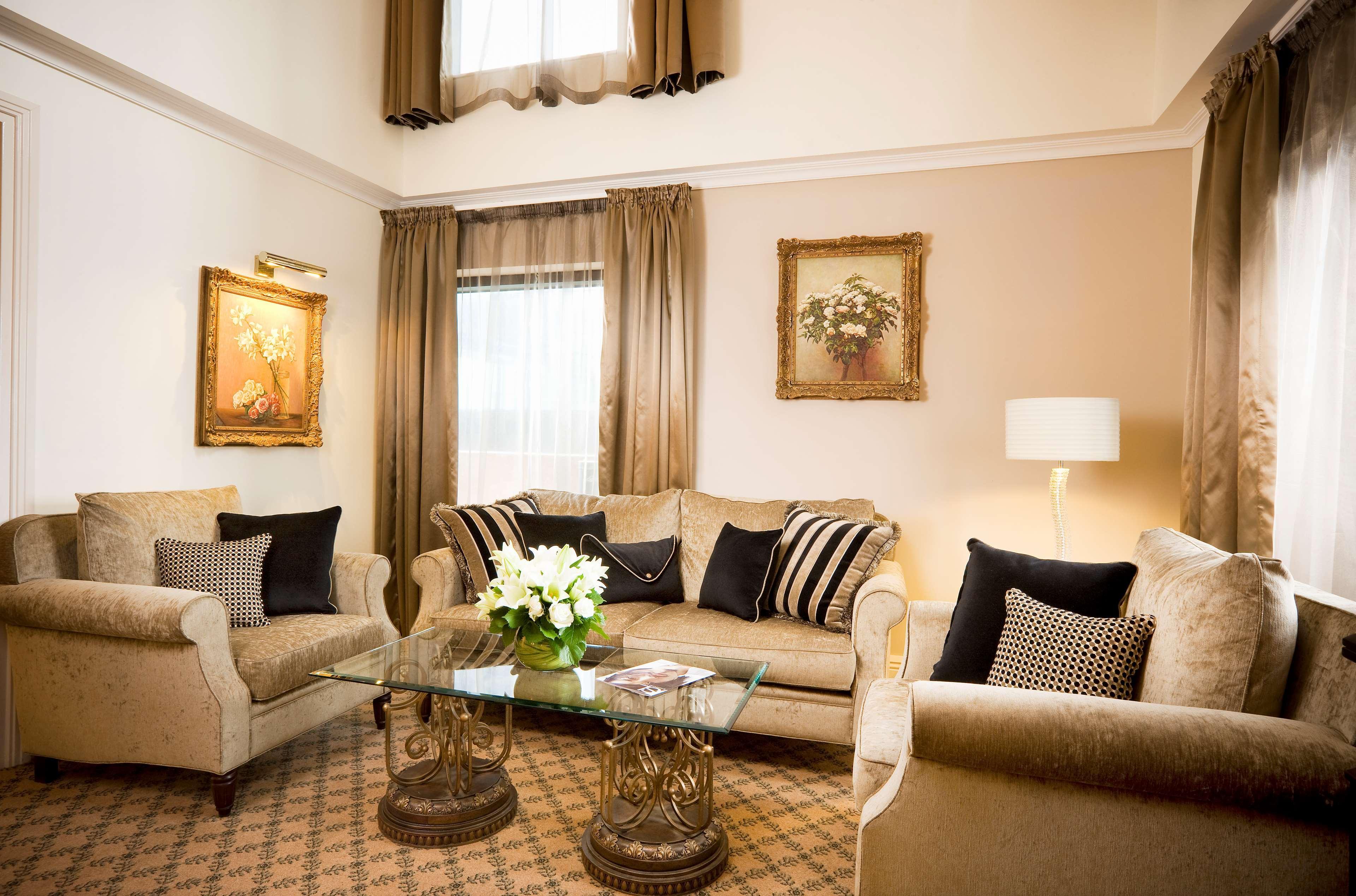 Stamford Plaza Melbourne Hotel Phòng bức ảnh The photo depicts a stylish living room with a warm and inviting aesthetic. It features a set of comfortable beige sofas adorned with decorative pillows in black and patterned designs. There is a glass coffee table at the center, supported by elegant