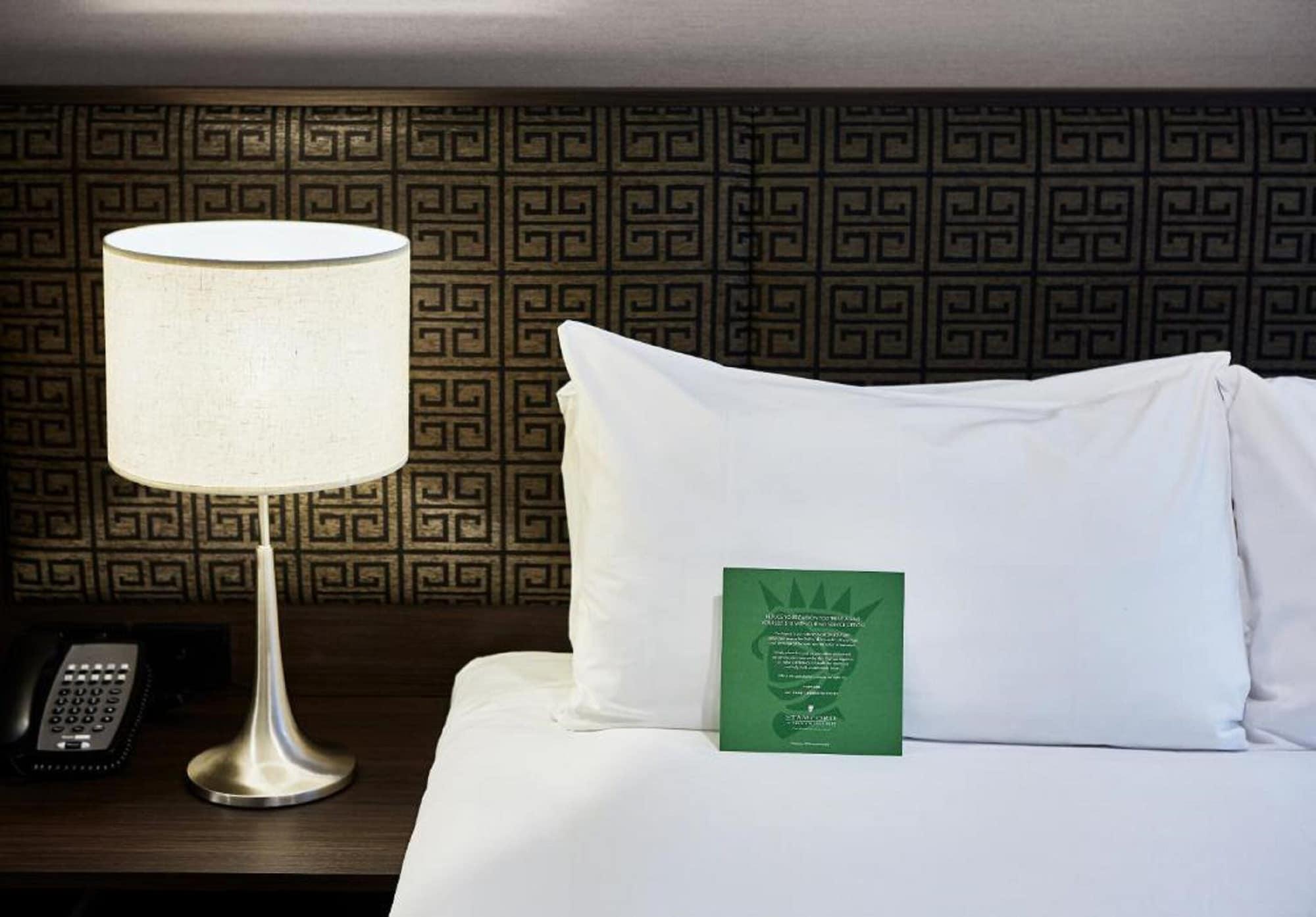 Stamford Plaza Melbourne Hotel Ngoại thất bức ảnh The photo shows a neatly made bed with a white pillow and a green item placed on top of it. Next to the bed, there is a stylish table lamp with a lampshade that appears to be white. In the background, you can see a patterned wall, which has a geometr