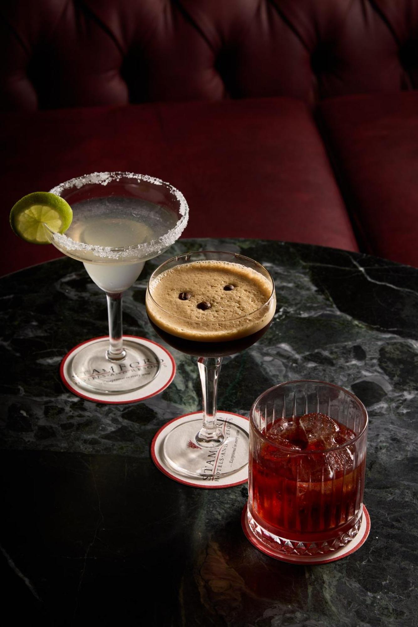 Stamford Plaza Melbourne Hotel Ngoại thất bức ảnh The photo displays three different cocktails arranged on a dark marble table. 

1. On the left, there is a margarita glass filled with a clear drink, garnished with a lime slice and featuring a salted rim.
2. In the center, a coupe glass holds a dark