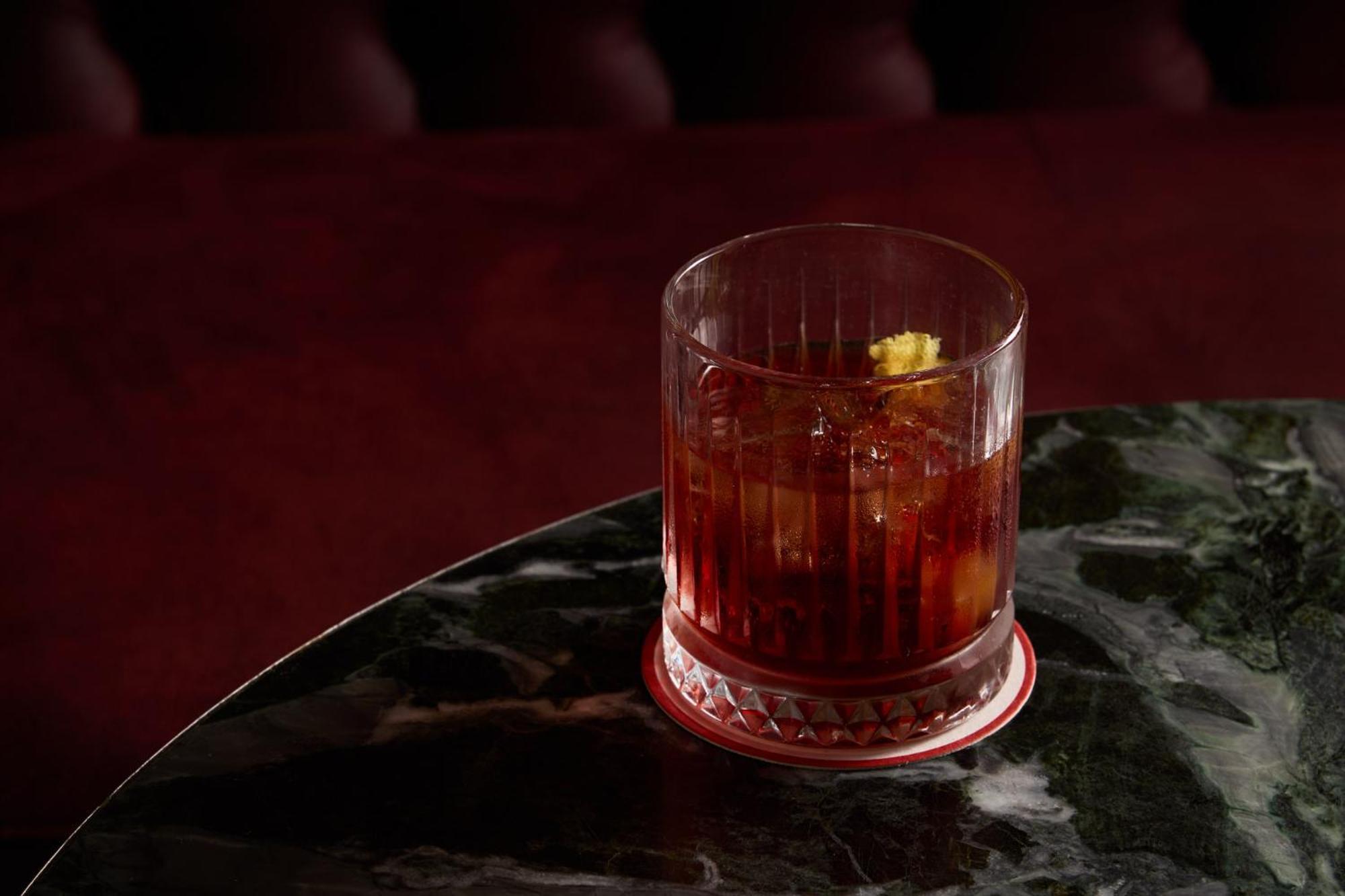Stamford Plaza Melbourne Hotel Ngoại thất bức ảnh The photo depicts a short glass filled with a dark-colored beverage, likely an alcoholic drink. The glass has a textured design, with ice cubes visible inside. A twist of lemon peel is perched on the rim, adding a touch of garnish. The drink sits on 