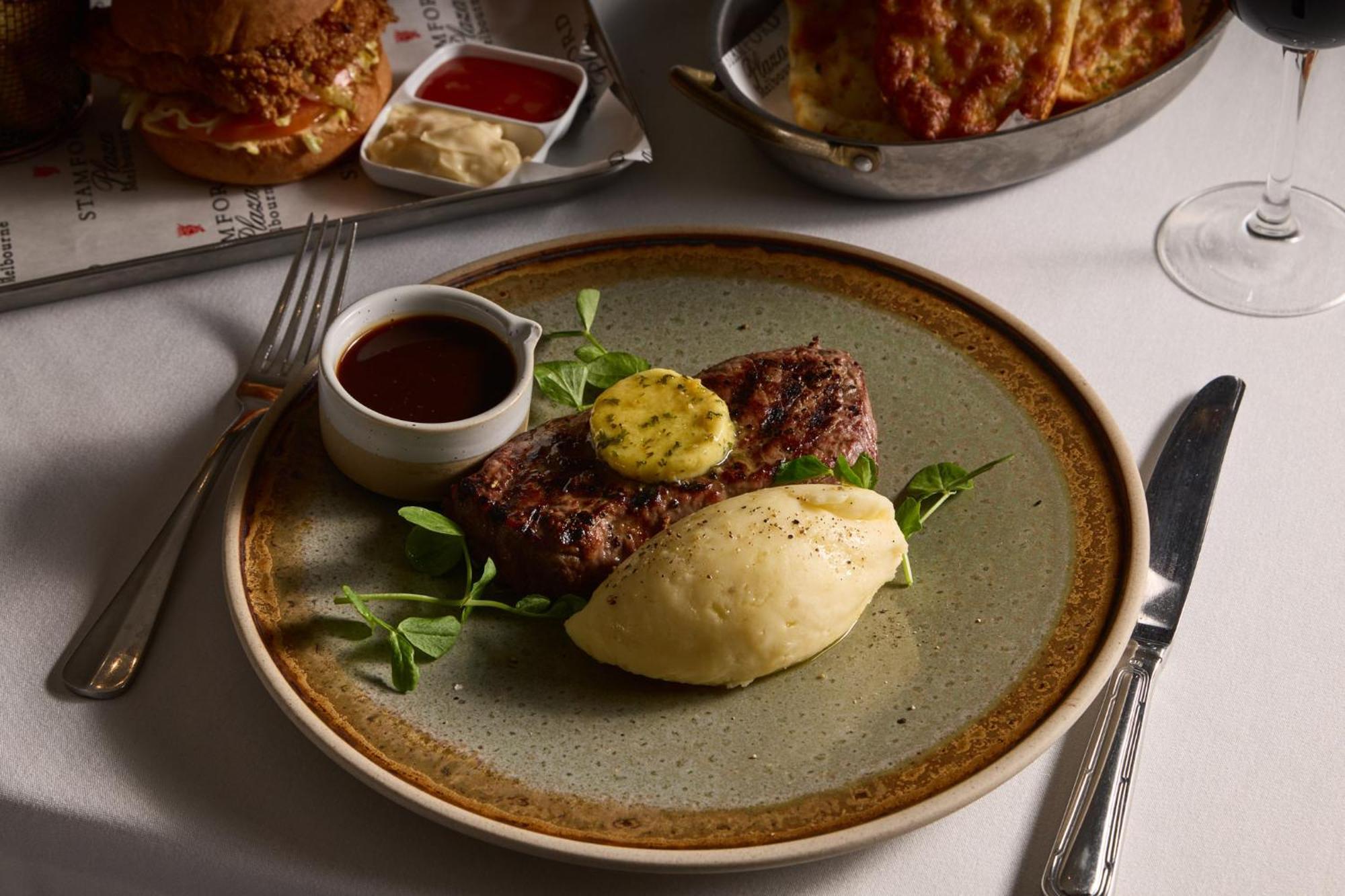 Stamford Plaza Melbourne Hotel Ngoại thất bức ảnh The photo shows a well-presented plate featuring a serving of steak, topped with a dollop of herb butter and surrounded by fresh sprouts or microgreens. There is a smooth portion of mashed potatoes beside the steak, and a small bowl of sauce, likely 