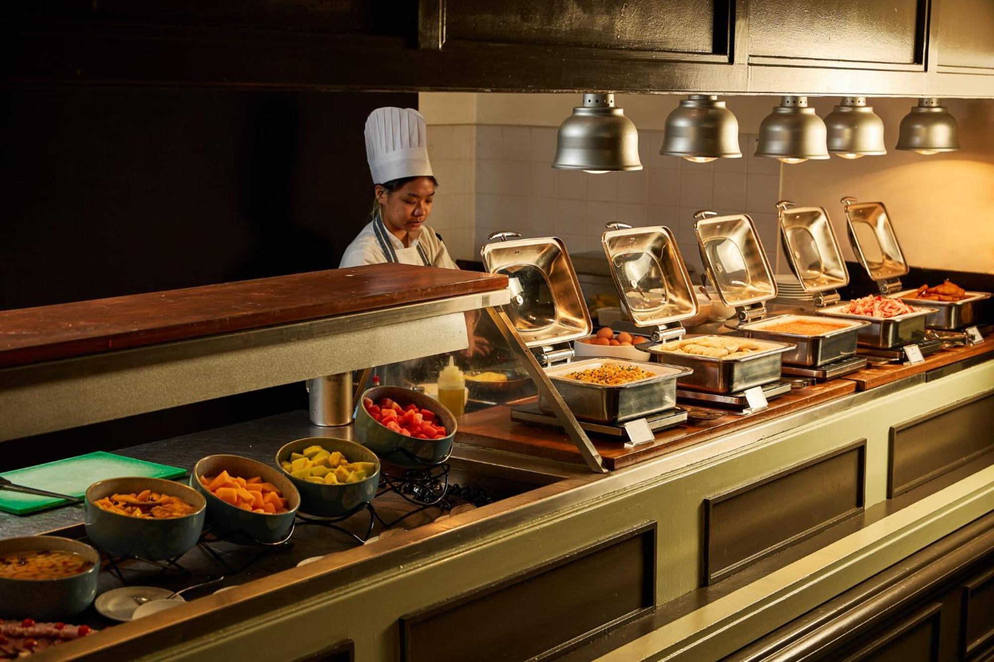 Stamford Plaza Melbourne Hotel Ngoại thất bức ảnh The photo shows a buffet setup in a dining area. There is a chef in a white uniform and hat, standing behind a counter filled with various food options. The buffet features several metal serving trays containing different dishes, with warming lights 