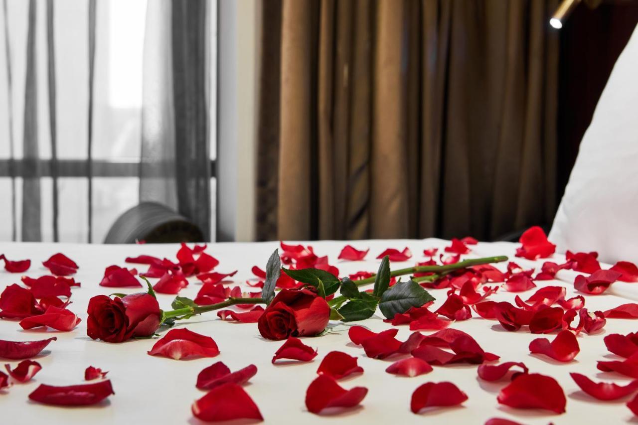 Stamford Plaza Melbourne Hotel Ngoại thất bức ảnh The photo shows a bed or a table covered with scattered red rose petals. Among the petals, there are a few whole red roses, still with their stems. The background features curtains that appear to be sheer, allowing some light to come through, and the